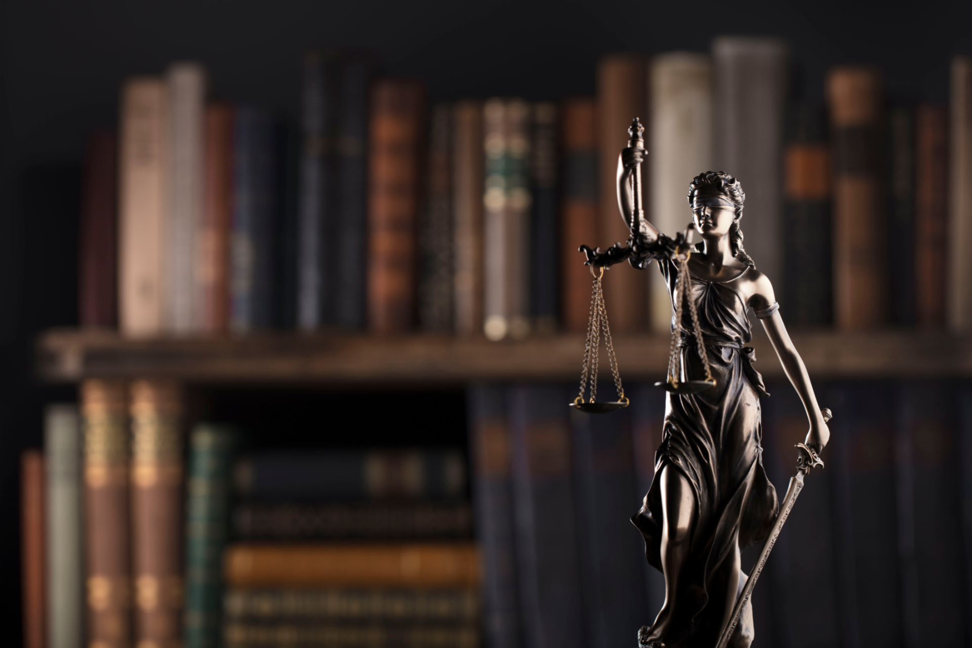 Statue of Lady Justice with scales and sword, in front of a bookshelf filled with books.