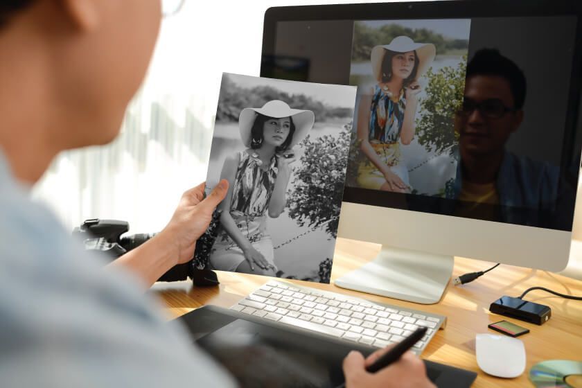 A person sitting at a desk holding a picture in front of a computer