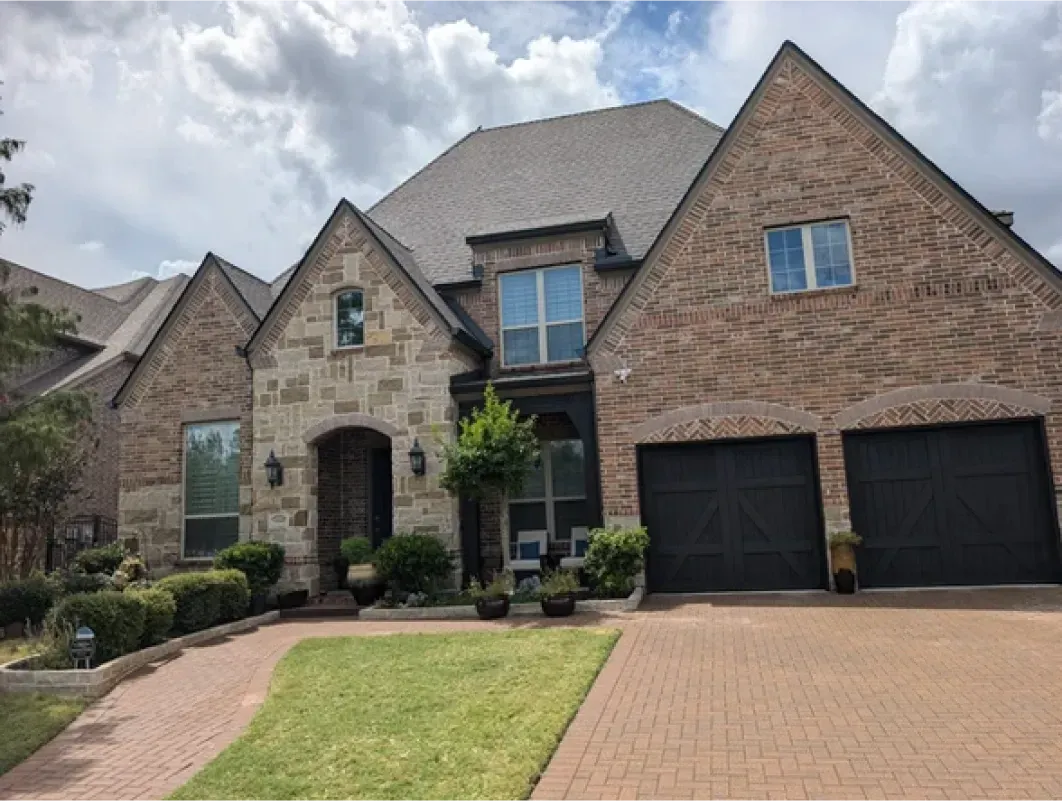 A large brick house with two black garage doors and a brick driveway.