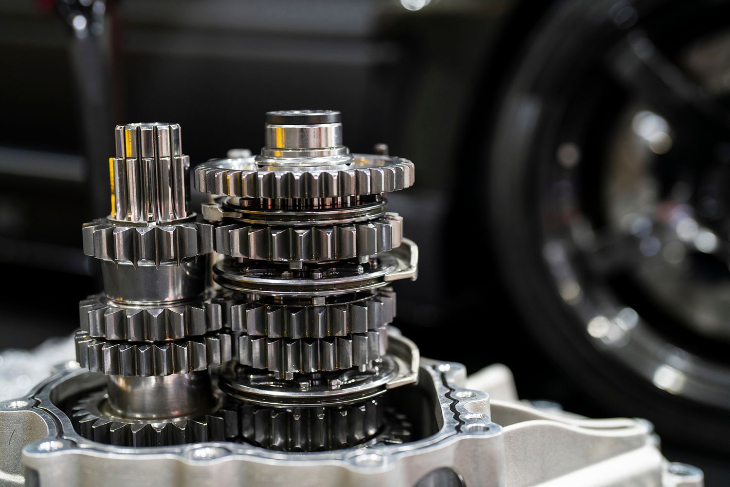 A close-up of gears of a car engine with a vehicle in the background.