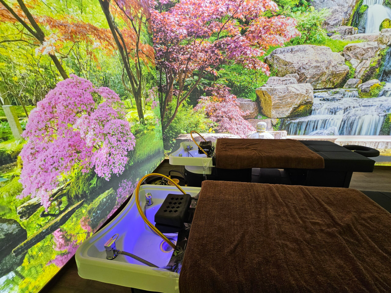 Due lettini per massaggi con asciugamani marroni di fronte a una cascata panoramica e a un murale raffigurante un albero in fiore.