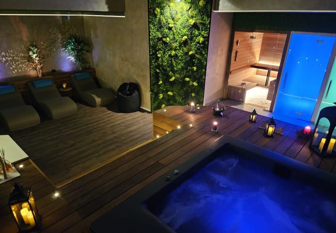 Area benessere con jacuzzi, sauna, lettini e candele decorative, illuminata con luce blu e gialla.