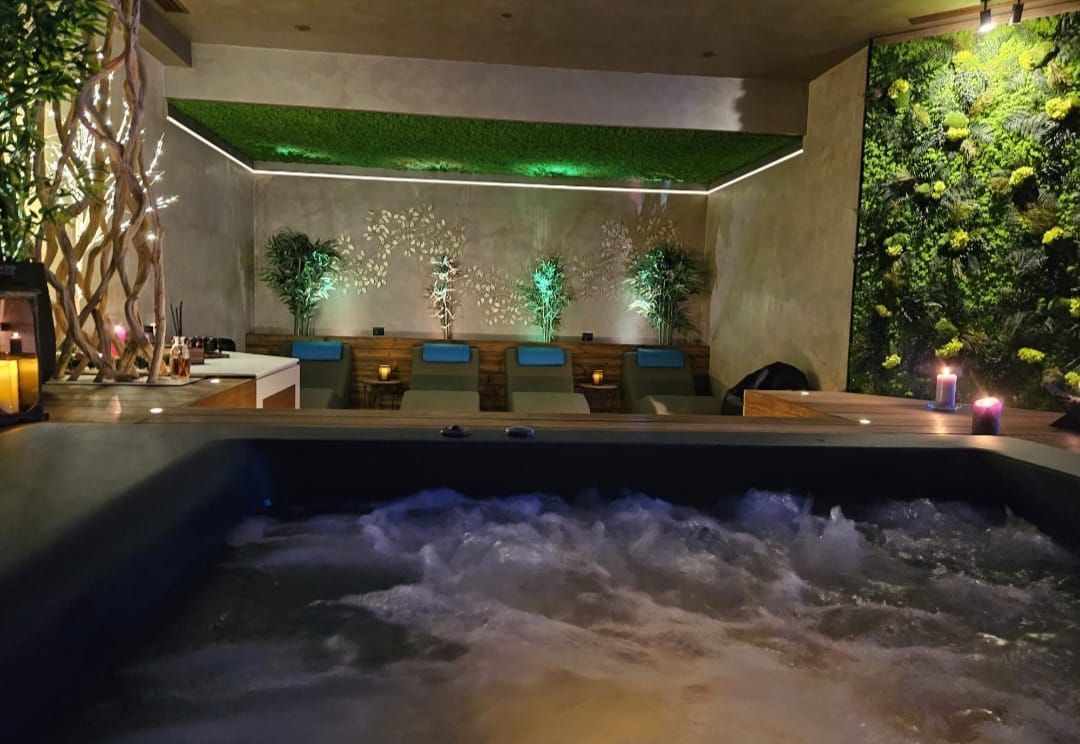 Vasca idromassaggio in una spa, con sedie a sdraio e una parete verde, nonché una parete strutturata con illuminazione decorativa.