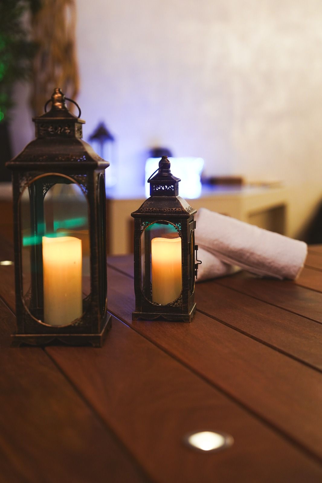Due lanterne a candela su un tavolo di legno con asciugamani arrotolati. Luce soffusa e calda.