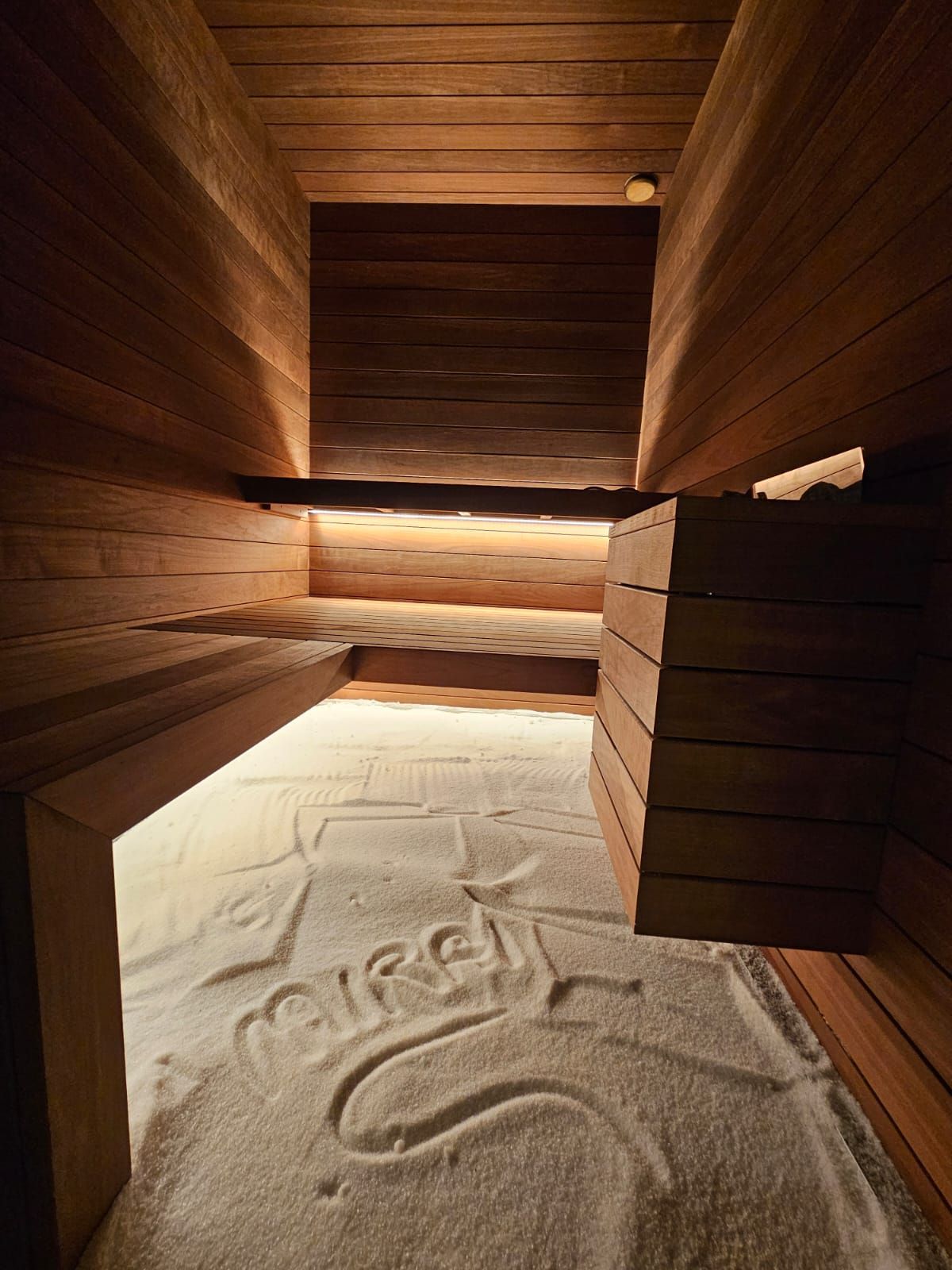 Interno della sauna in legno, pavimento in sabbia con la scritta