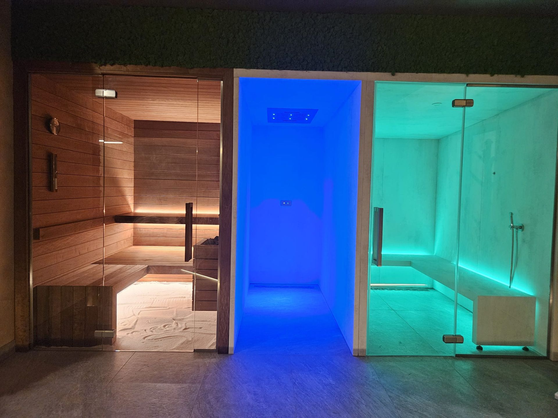 Sauna con pannelli in legno, bagno turco con luce blu e bagno turco con luce verde e porte in vetro.