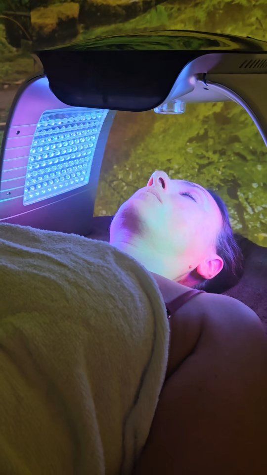 Donna sottoposta a trattamento di terapia con luce LED, viso illuminato da luce blu e colorata.