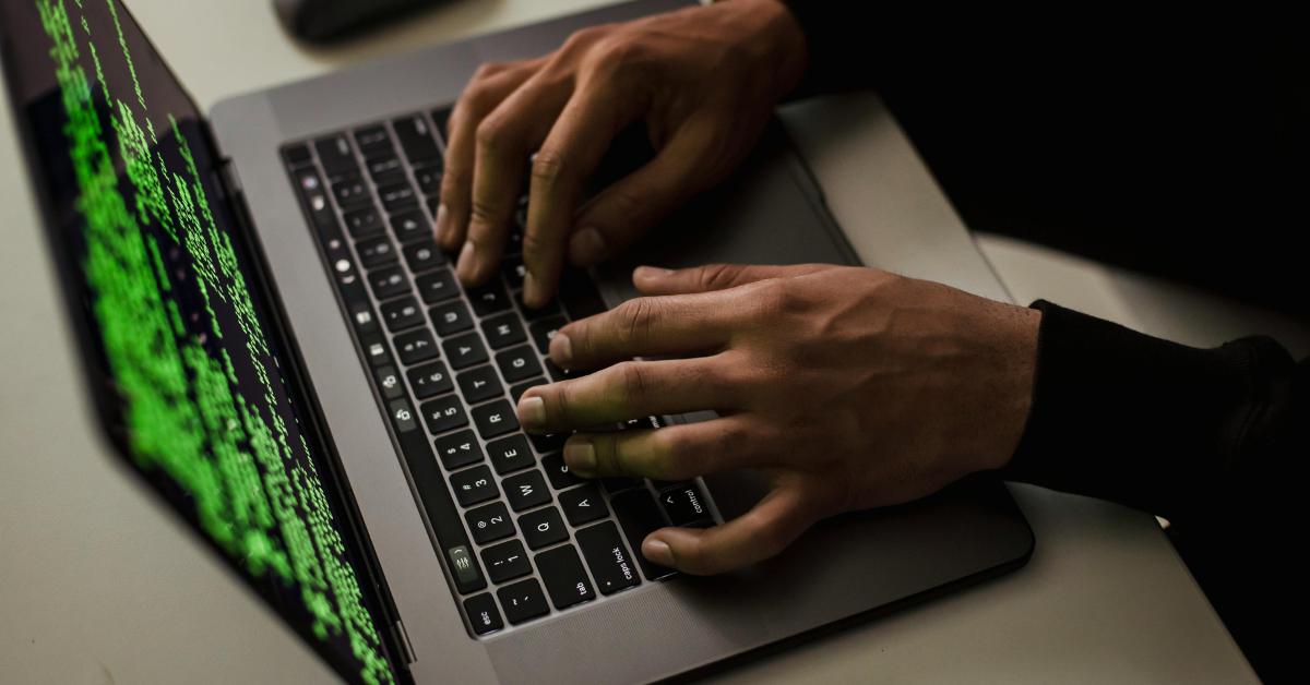 Hands typing on a laptop with green code on the screen