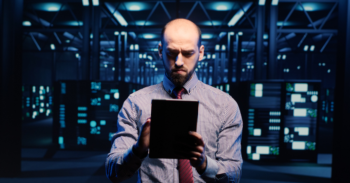 Man using a tablet in a data center surrounded by servers.