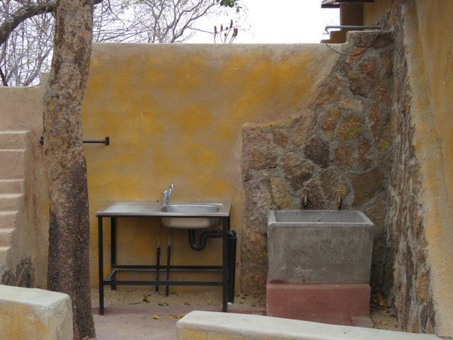 Outdoor sink area: yellow stucco wall, stone detail, stainless steel sink, concrete basin, steps.