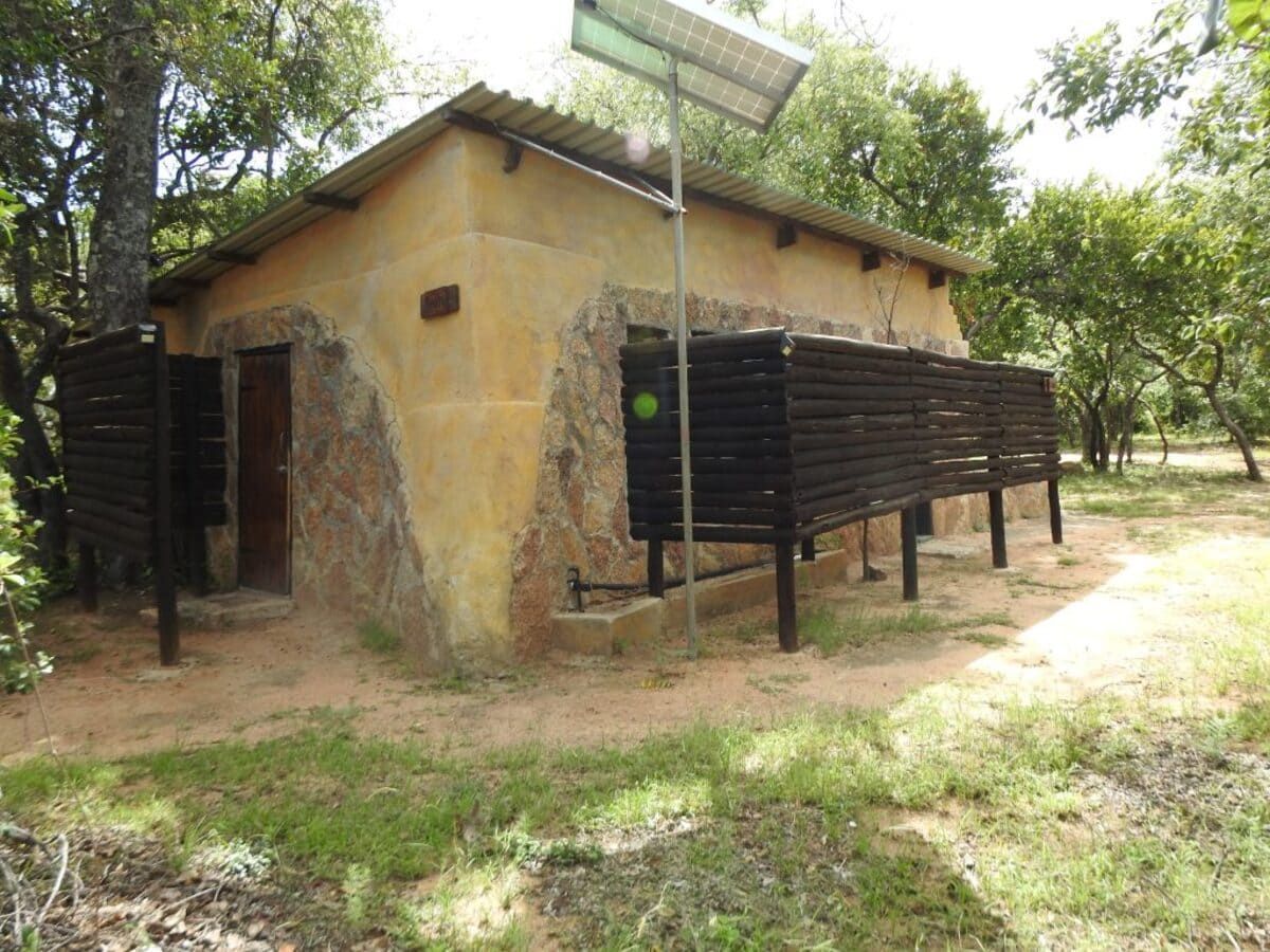 Small tan building with solar panel, wooden privacy screens, and surrounded by trees.