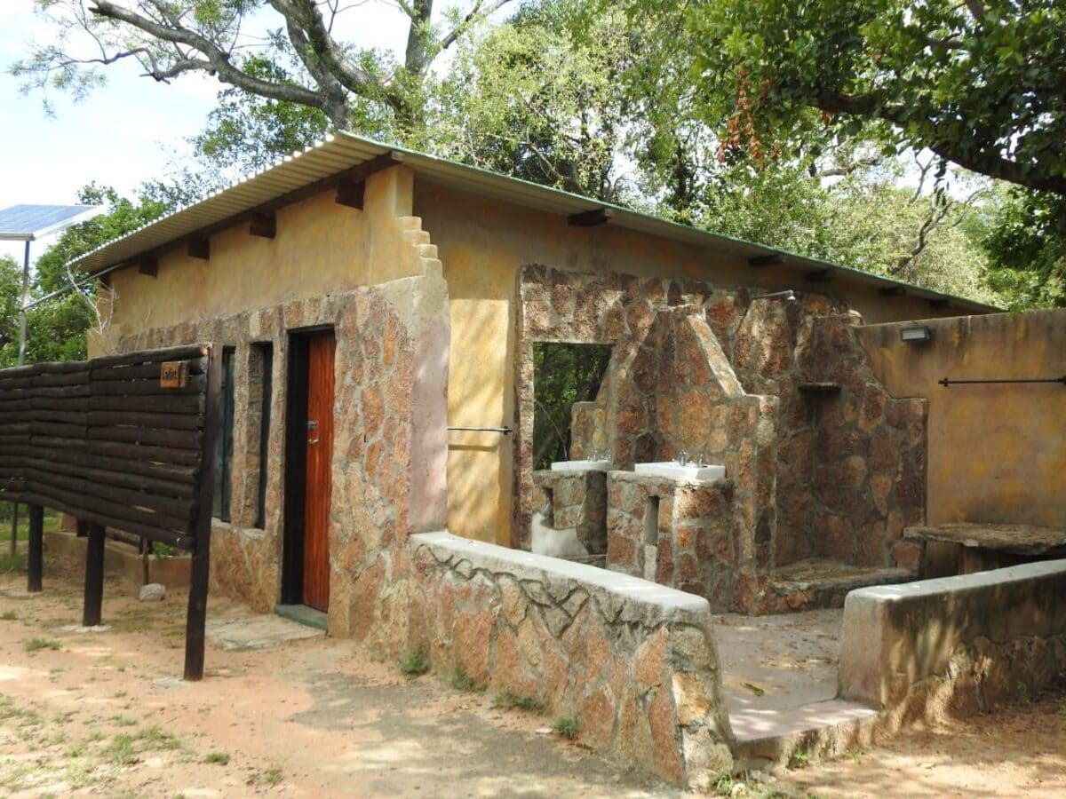 Stone and tan building with a sloped roof and open doorway; set outdoors, likely in a park.