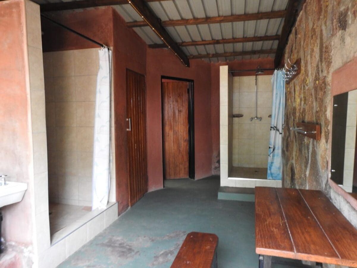 Interior of a rustic bathroom with shower stalls, wooden door, and benches.