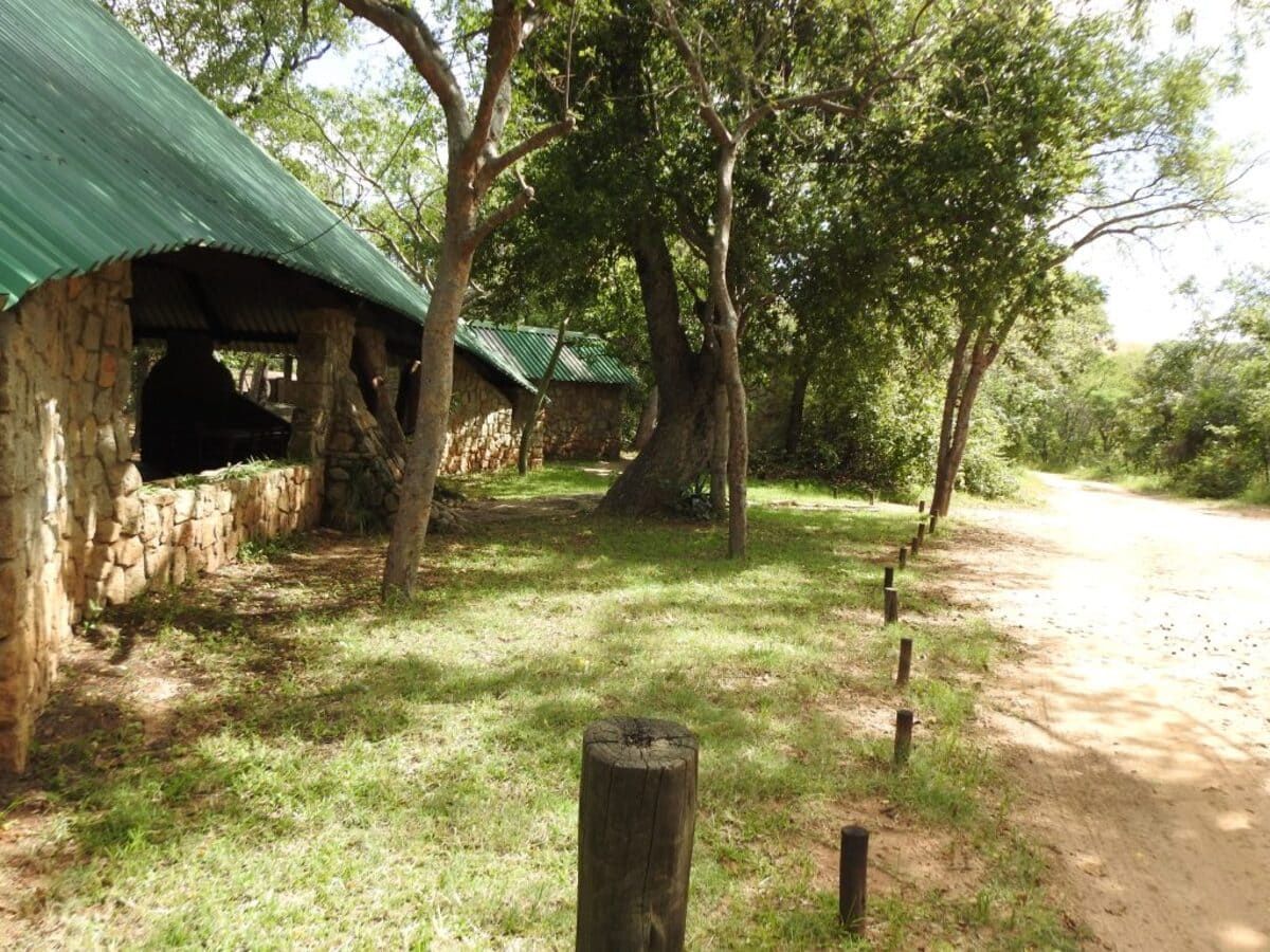 Stone buildings with green roofs and trees beside a dirt road.