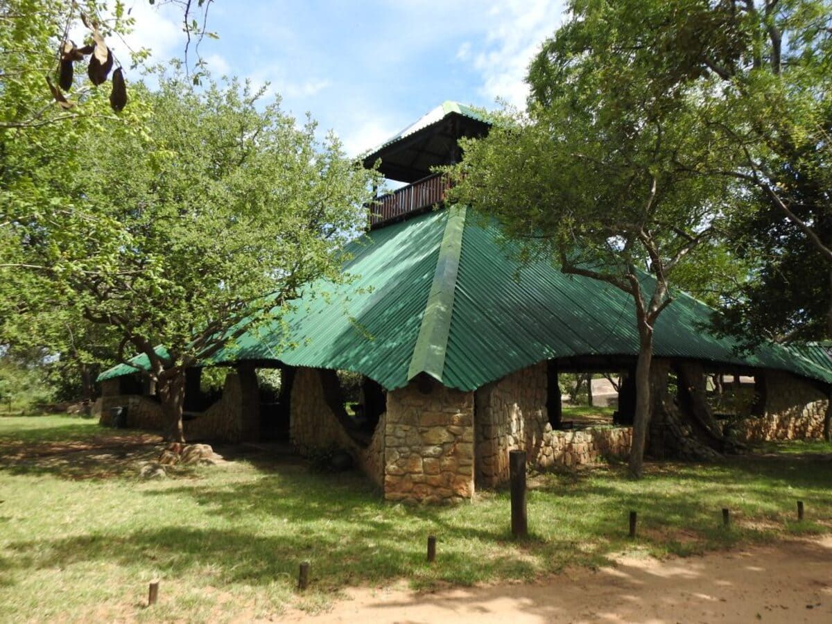 Stone building with green roof and viewing platform surrounded by trees.