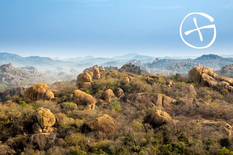 Hilly landscape with large boulders and a hazy sky; logo in the upper right.