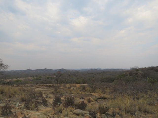 Dry, brown landscape under a cloudy sky. Sparse vegetation and distant, rolling hills.