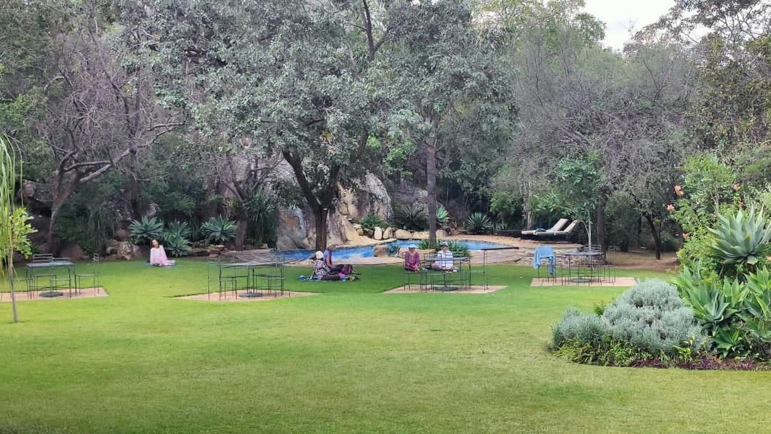 Grassy park with trees, a pool, and people relaxing at tables.