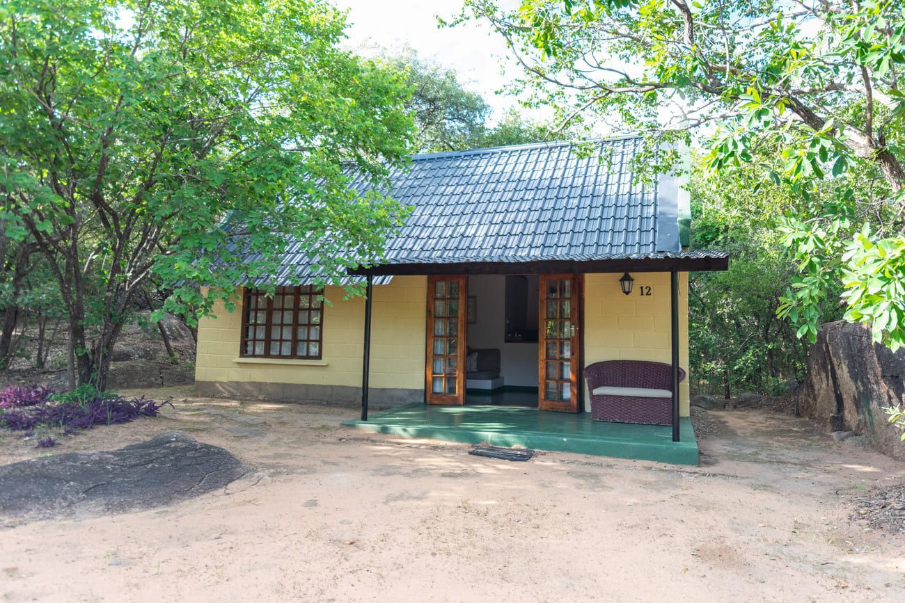 Small yellow cabin with dark roof, surrounded by green trees and foliage.