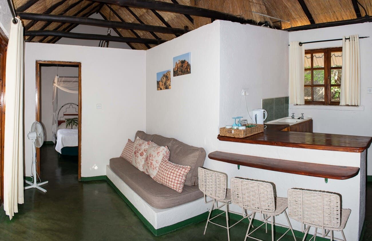 Interior of a white-walled room with a sofa, bar counter, and view into a bedroom.