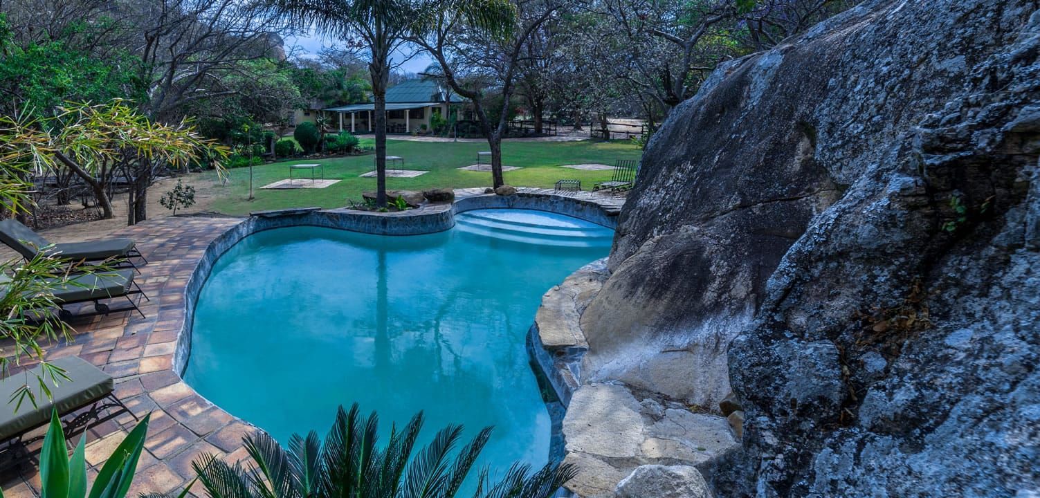 A scenic pool with a rocky waterfall, surrounded by trees and green lawns.