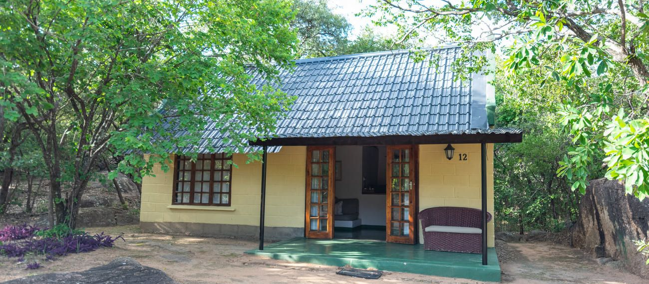 A small, yellow cottage with a tiled roof and open double doors in a natural setting.