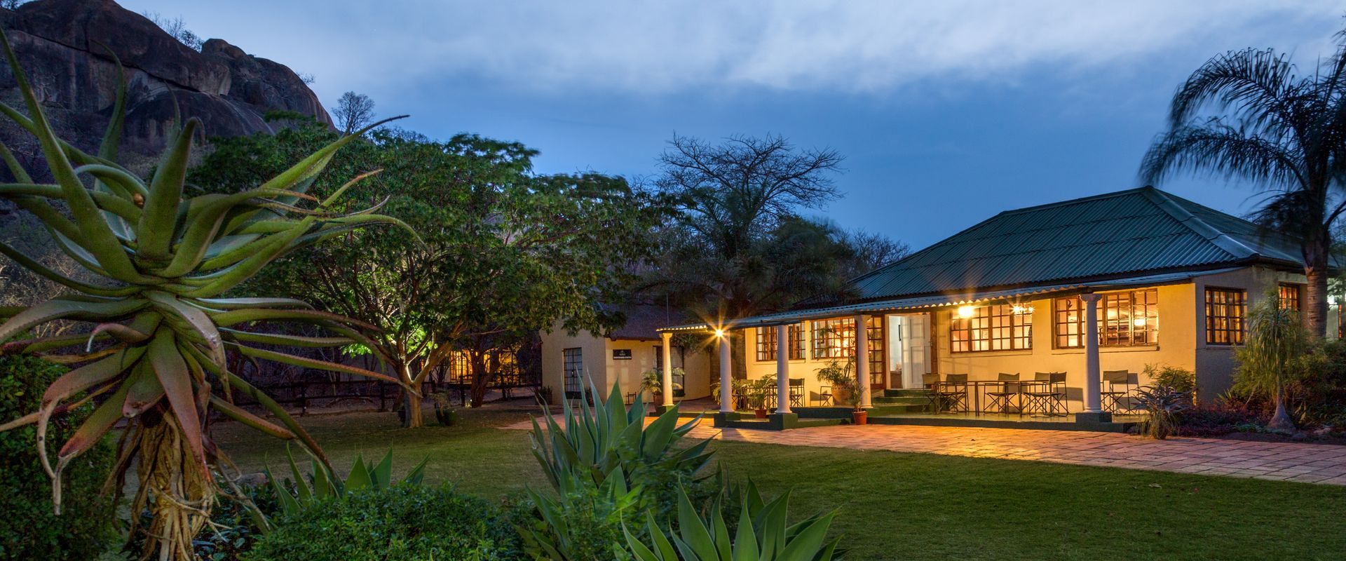 Small beige cottage with a dark-tiled roof, surrounded by trees in a natural setting.