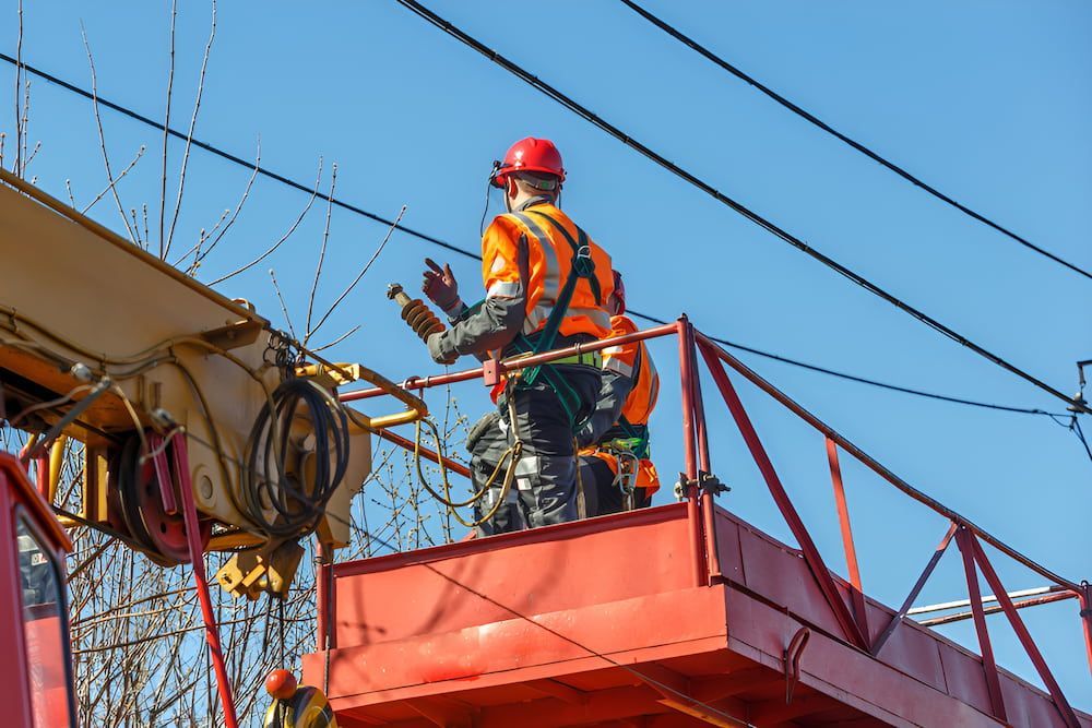 A Man Is Standing On Top Of A Crane Working On Power Lines — In-Line Electrical Southern Highlands in Marulan, NSW
