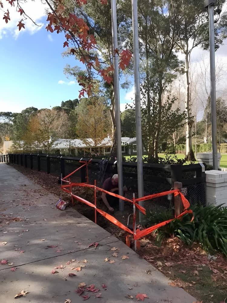 A Man Is Working On A Fence In A Park — In-Line Electrical Southern Highlands in Carrick, NSW