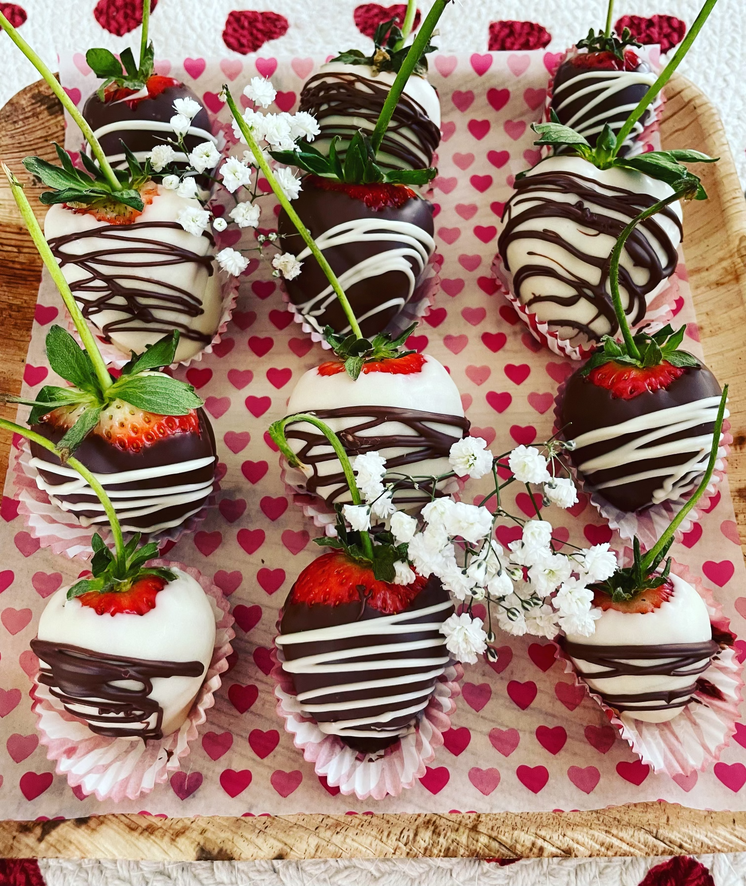 A wooden tray filled with chocolate covered strawberries and baby 's breath.