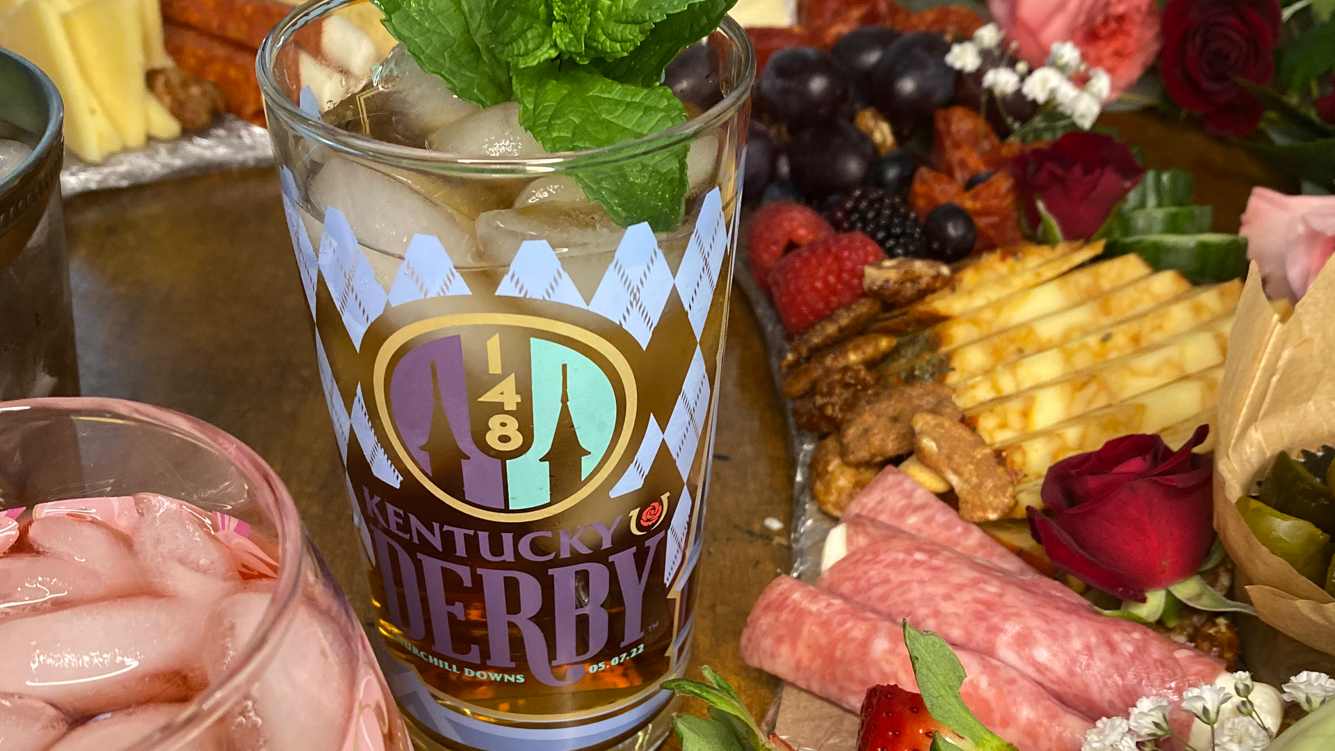 A glass of kentucky derby is sitting on a table next to a plate of food.