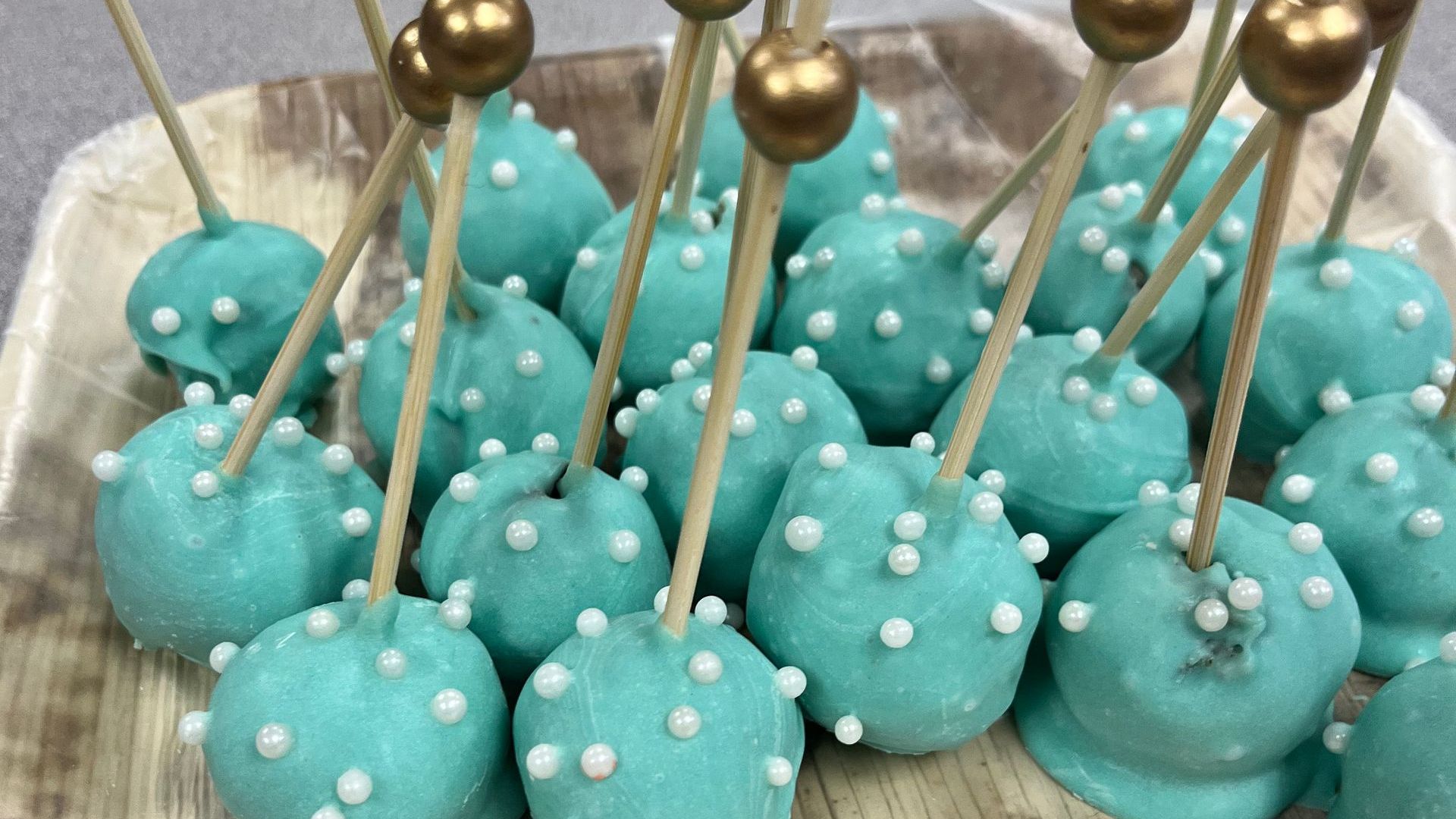 A bunch of blue cake pops with white sprinkles on sticks on a plate.