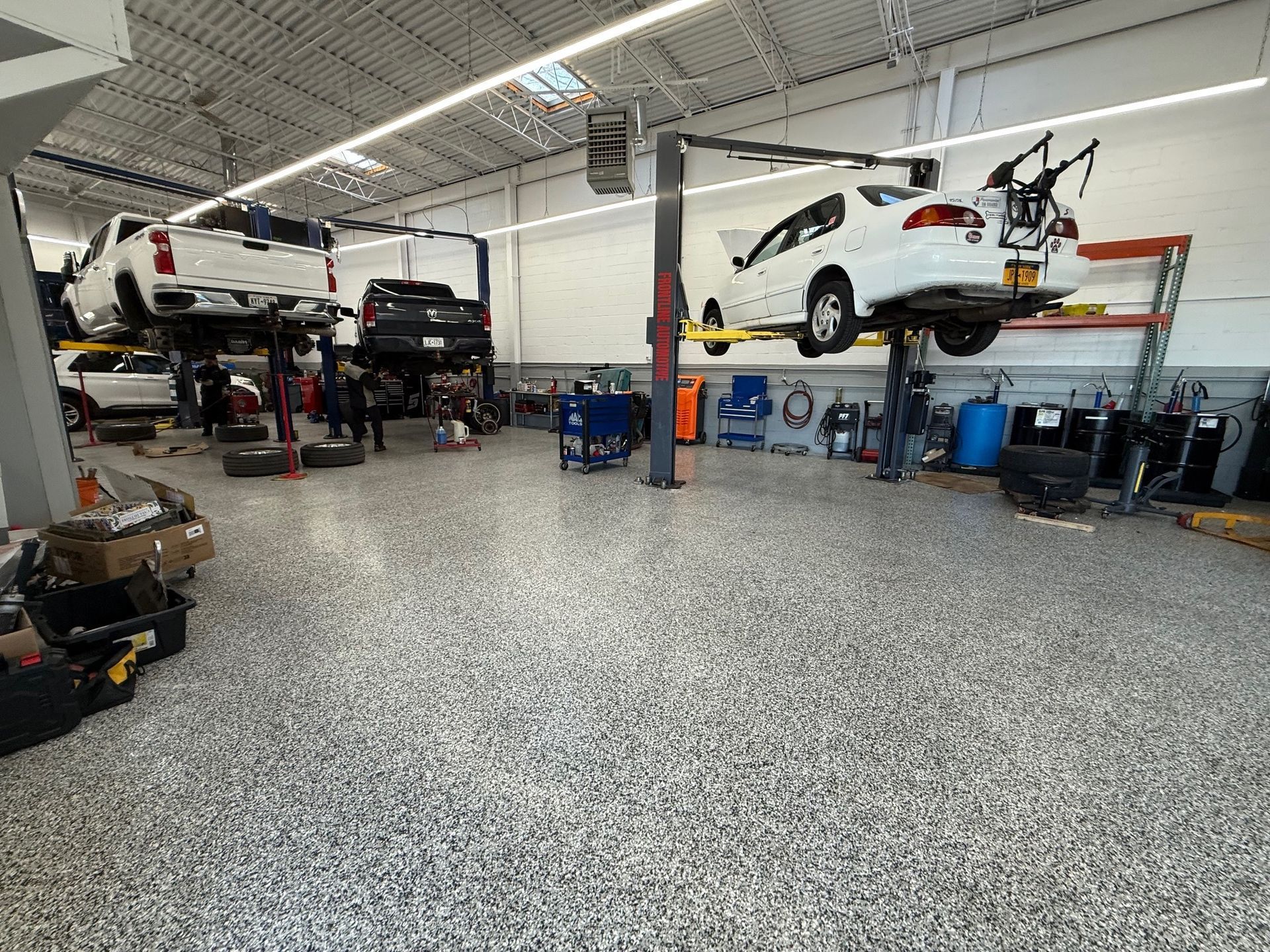 A brightly lit auto repair shop with two white cars on lifts and a dark truck parked in a service bay.