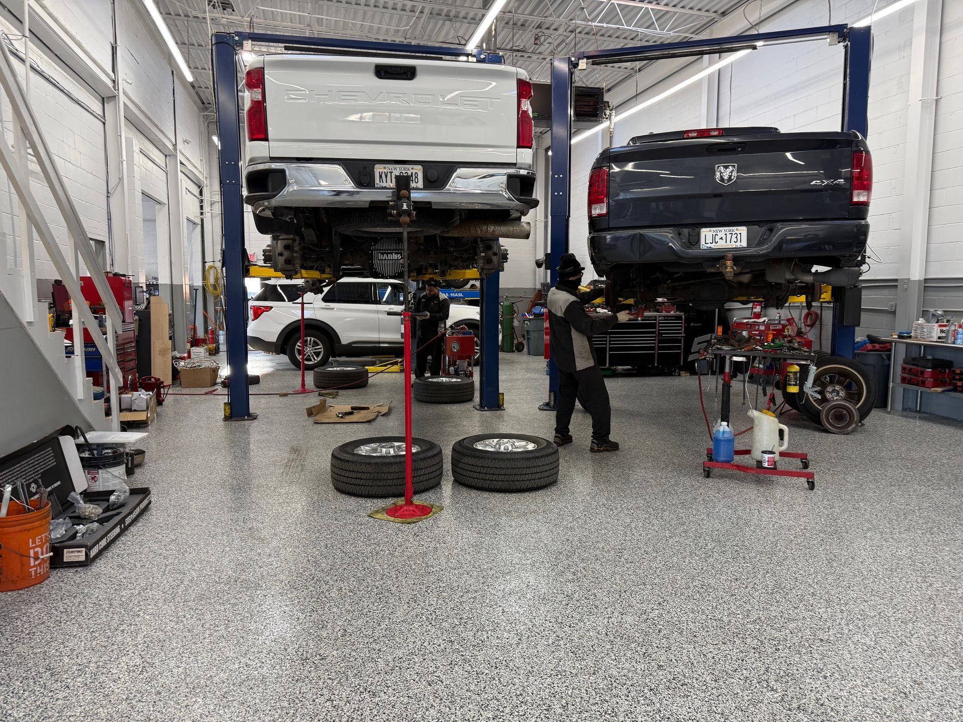 Two pickup trucks raised on hydraulic lifts in a brightly lit automotive repair shop with a technician working nearby.