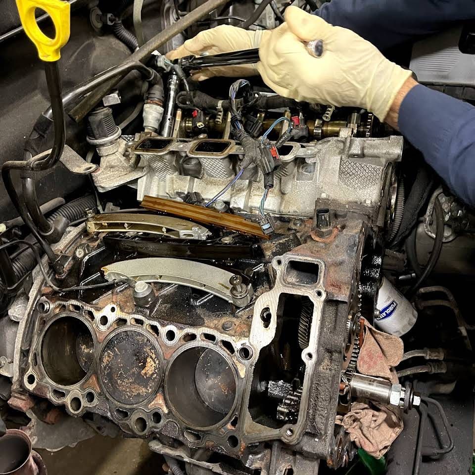 A mechanic in gloves points at a car engine with exposed pistons, in a garage setting. | Frontline Auto Repair