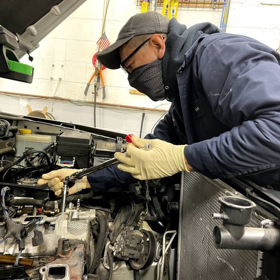 Mechanic wearing mask and gloves works on a car engine in a garage. | Frontline Auto Repair