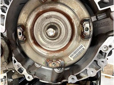 Close-up of a transmission component; circular metal piece with bolts attached, inside a metal casing. | Frontline Auto Repair