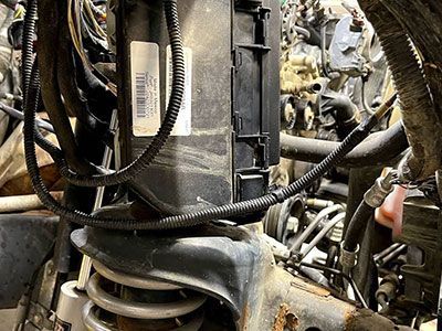Black box with wires, mounted near a vehicle's suspension coil.  Complex engine parts in background. | Frontline Auto Repair