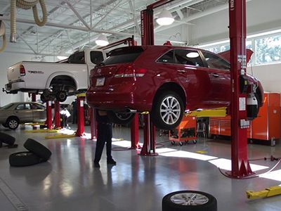 Cars on lifts in a bright auto shop; a mechanic works beneath one. | Frontline Auto Repair
