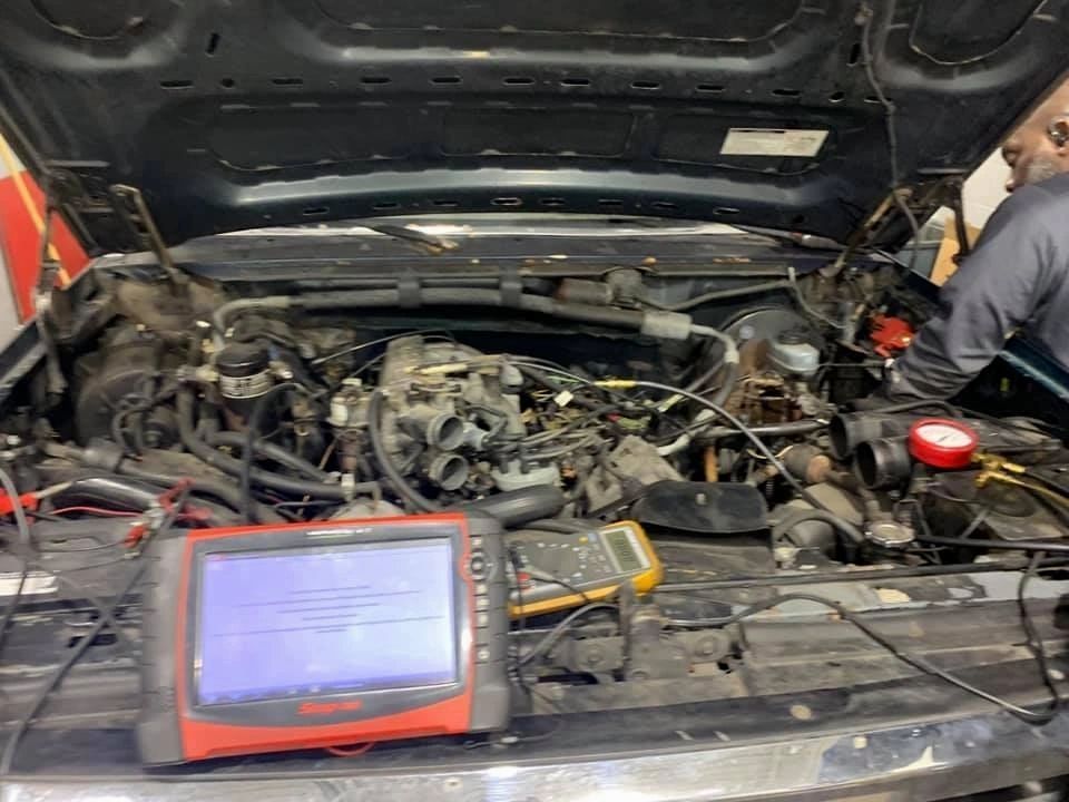 Mechanic working on car engine, using a diagnostic tool. Engine bay open. | Frontline Auto Repair