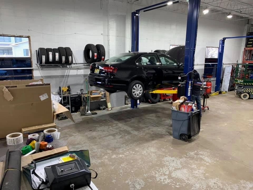 Car on a lift in a garage. A mechanic is working on it. Tires and tools are visible. | Frontline Auto Repair