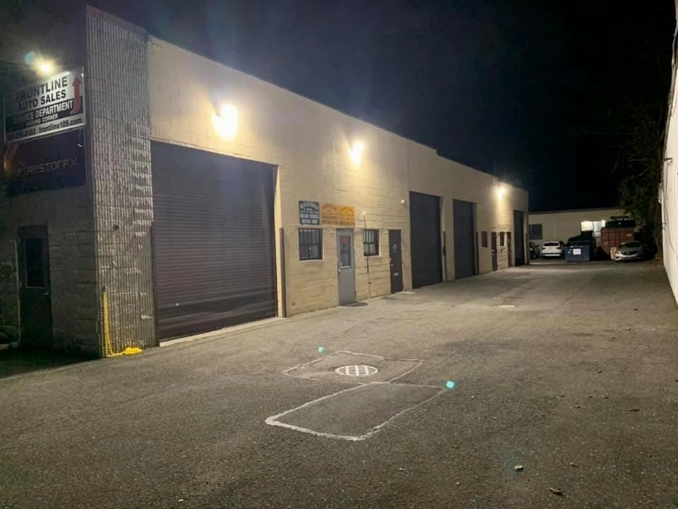 Exterior of a commercial building at night; several closed garage doors and parked cars. | Frontline Auto Repair
