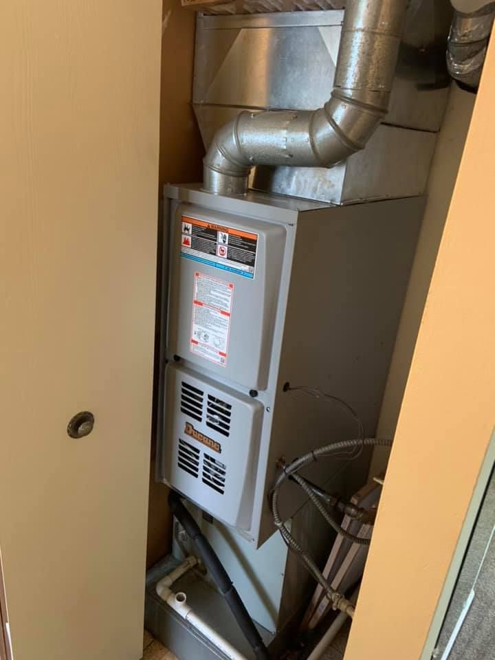 A grey HVAC furnace unit installed inside a closet, with metal ductwork extending from the top.