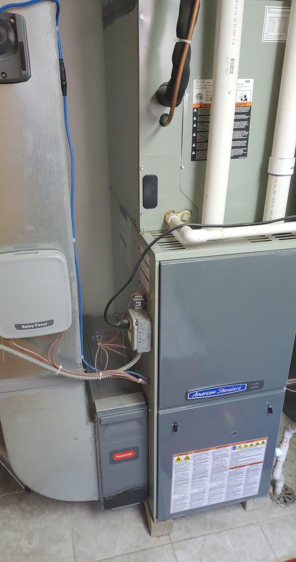 A gas furnace and evaporator coil unit with metal ductwork, white PVC venting pipes, and electrical connections.