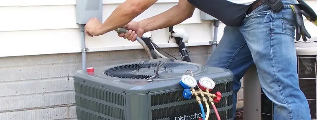 A technician working on an outdoor HVAC unit, connecting a gauge manifold to the system.
