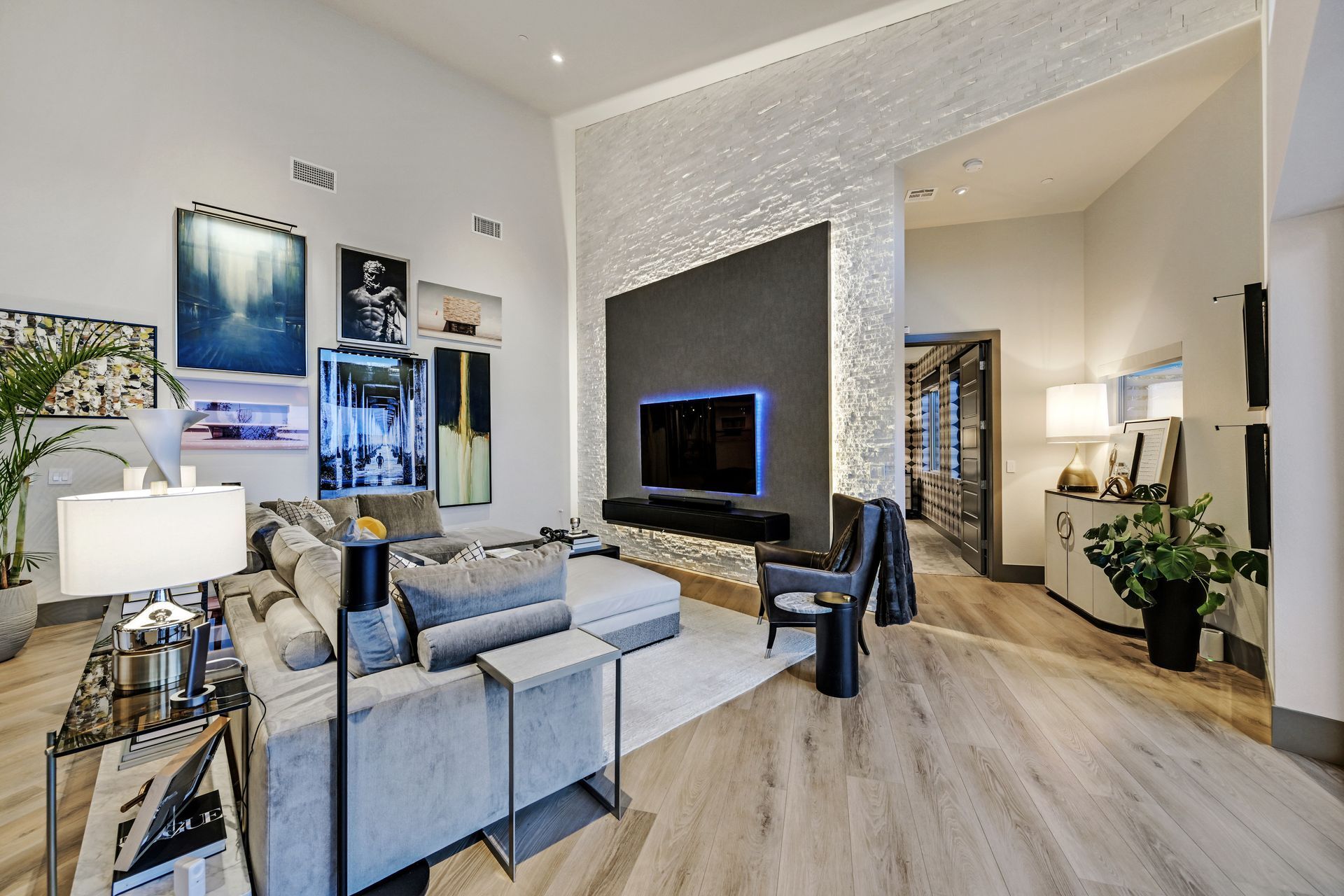 Modern living room with artwork, large TV, and sectional sofa; light wood floors, and textured accent wall.