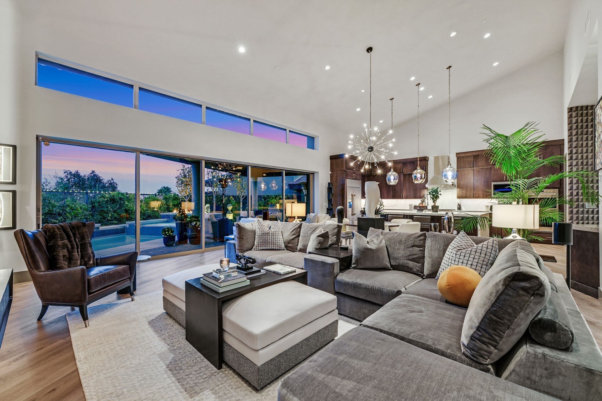 Spacious modern living room with gray sectional, large windows, and open kitchen.