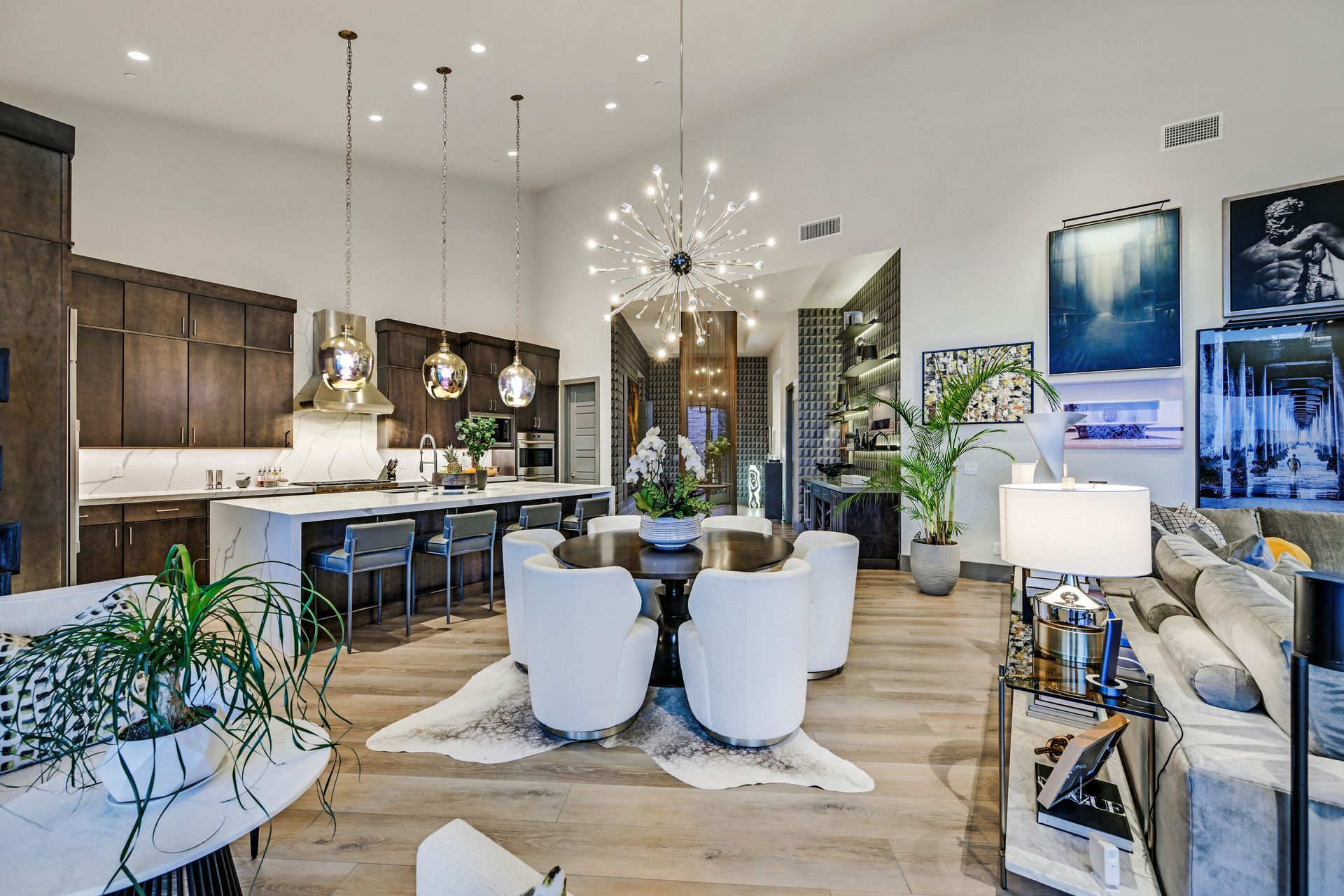 Open-concept kitchen and dining area with high ceilings, dark cabinets, a large island, and contemporary decor.