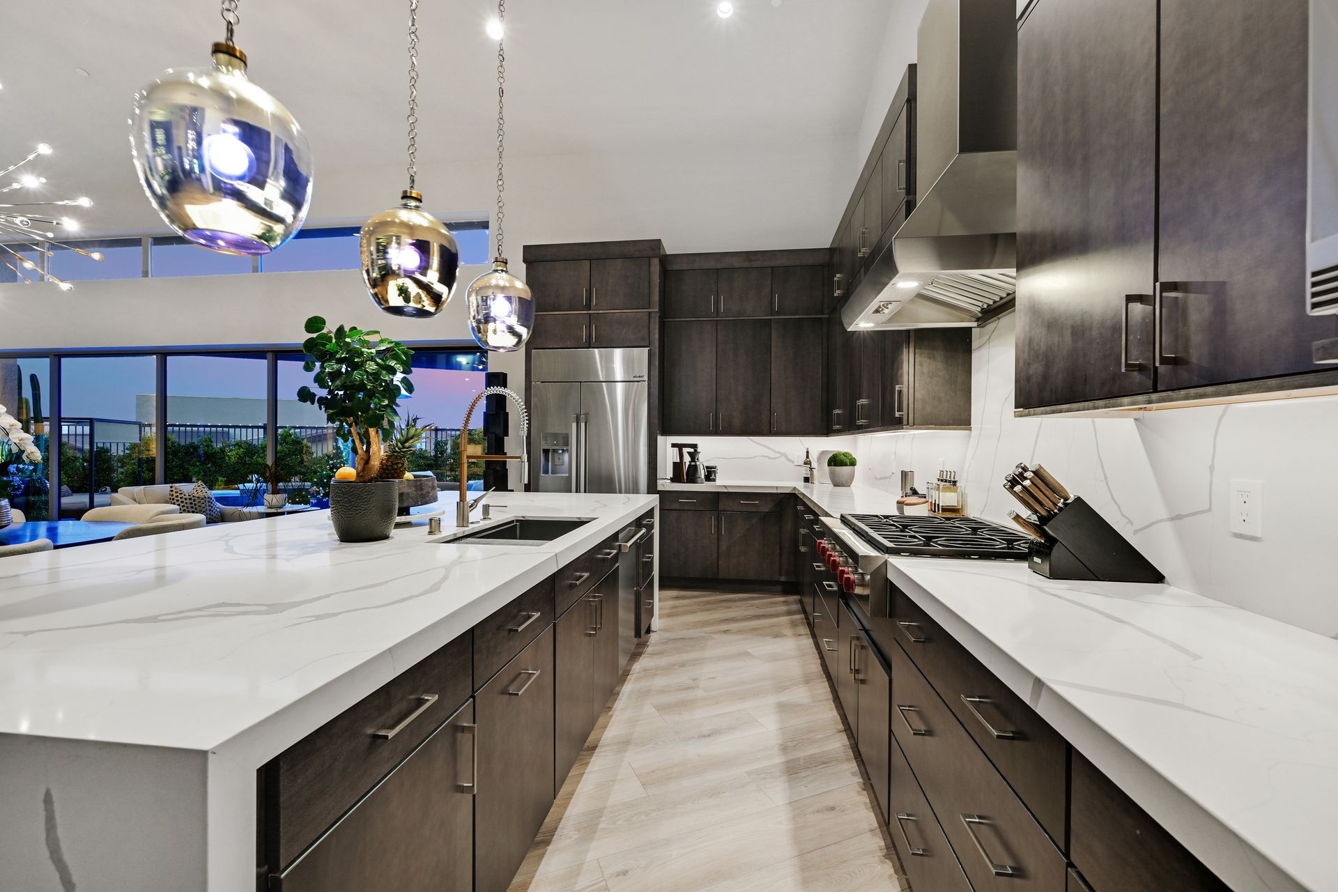 Modern kitchen with dark cabinetry, white countertops, stainless steel appliances, and pendant lights.