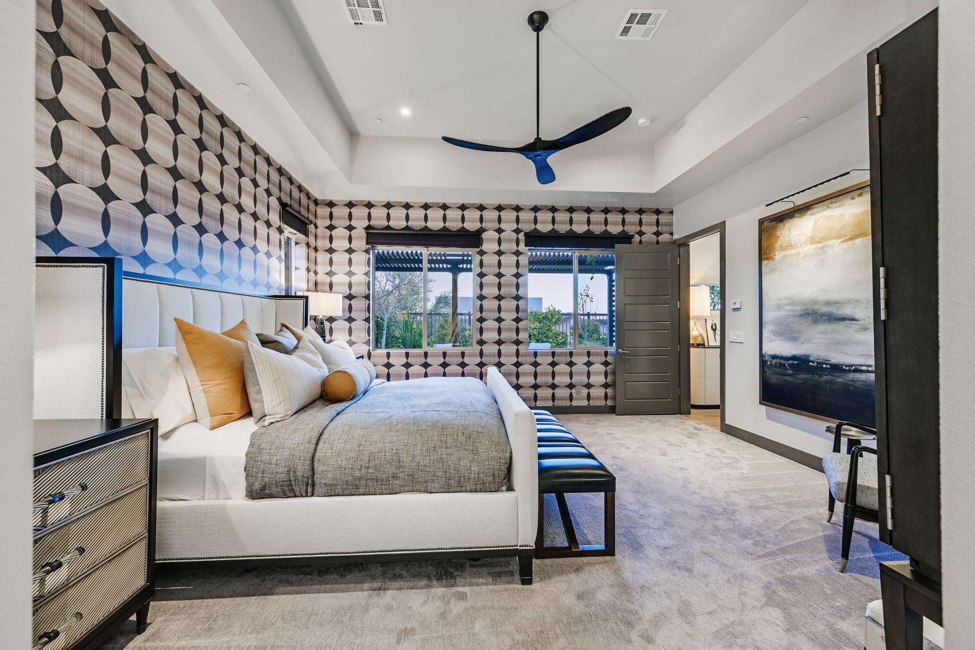 A modern bedroom with patterned wallpaper, a white bed, and a blue ceiling fan.